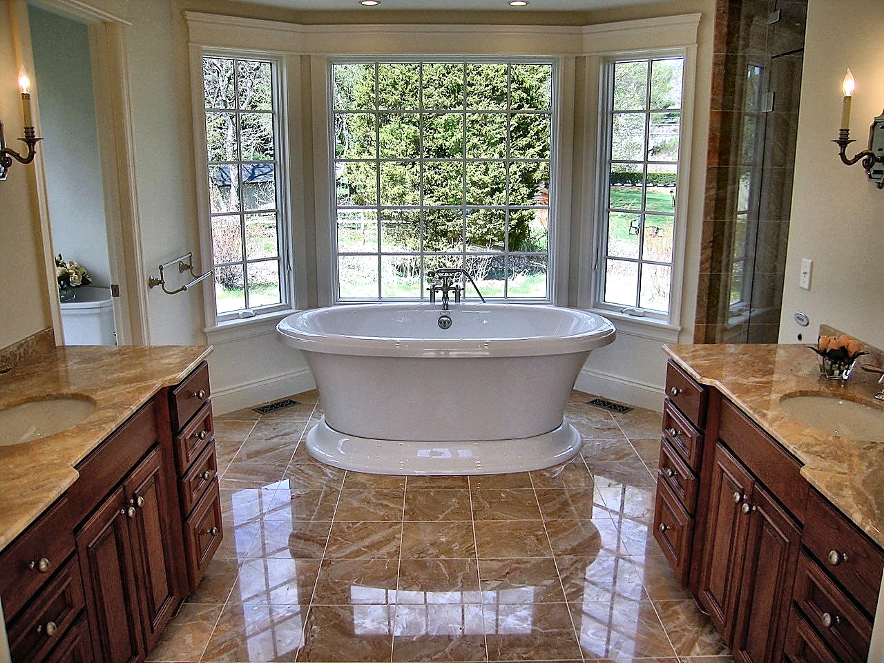 Bath with a pedestal tub in a bay window between twin cherry vanities