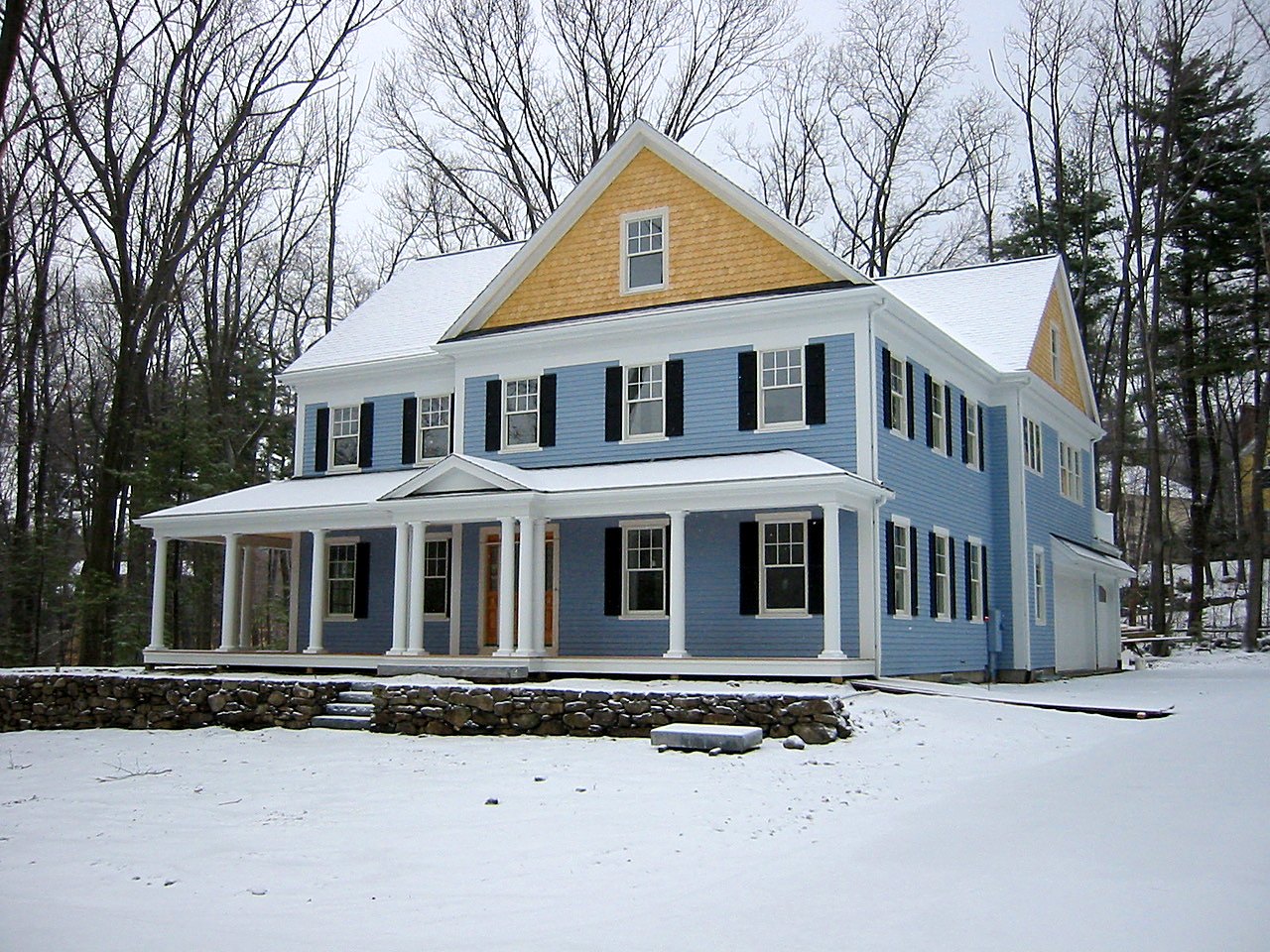 Blue colonial with a cedar-shingled gable and columned porch after a fresh snowfall