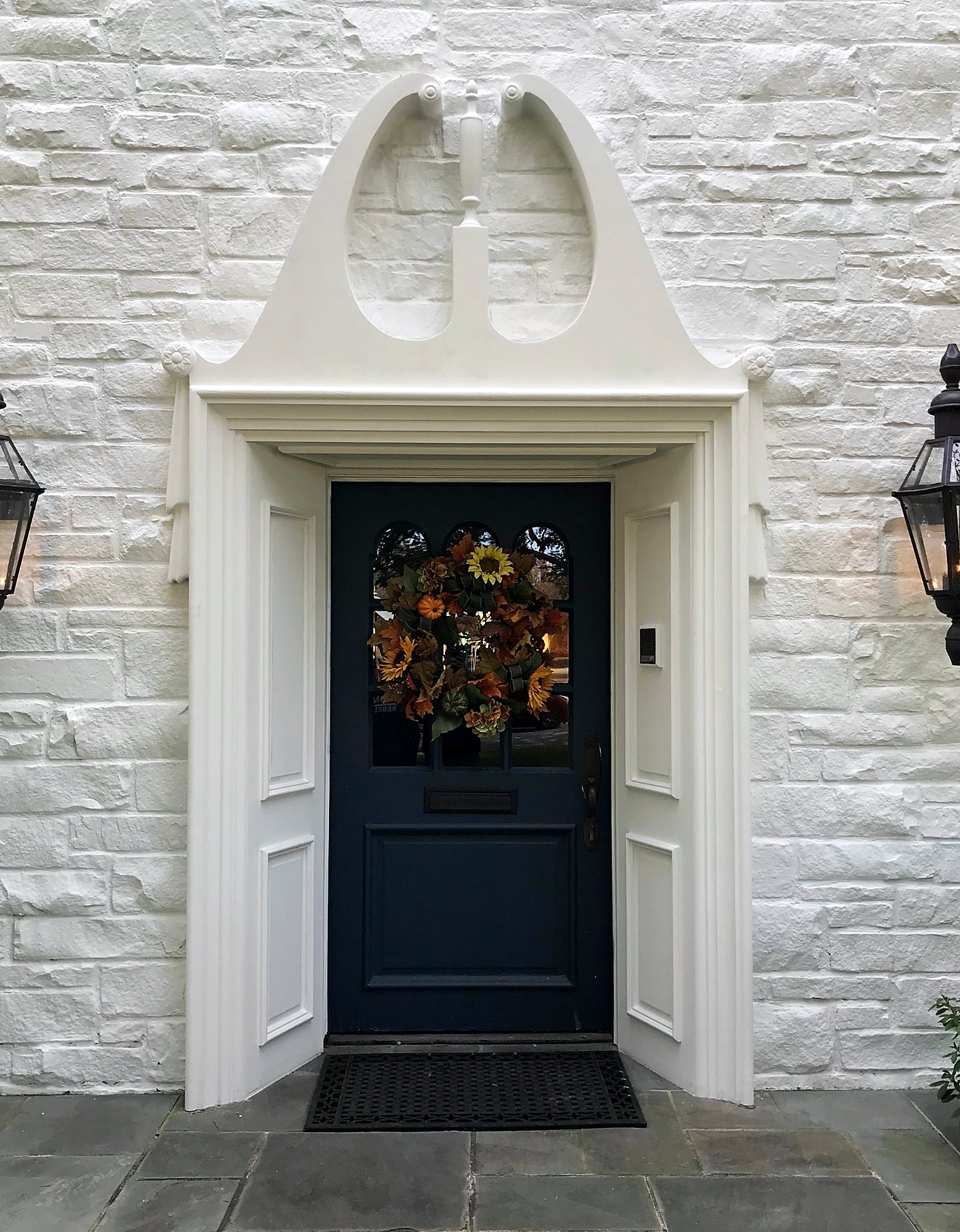 Classical entry with a broken-pediment door surround, paneled reveals and gas lanterns on painted stone