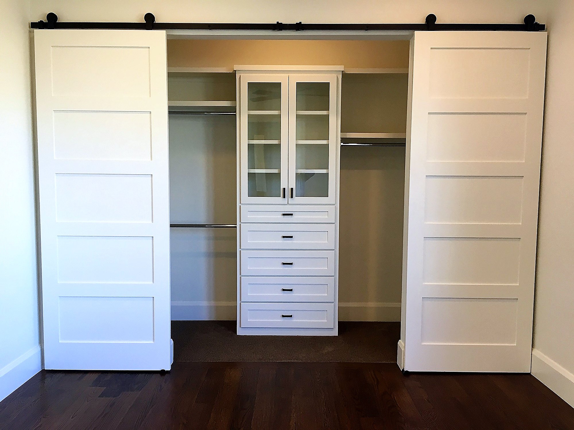 Closet system with glass-front cabinet framed by twin sliding barn doors