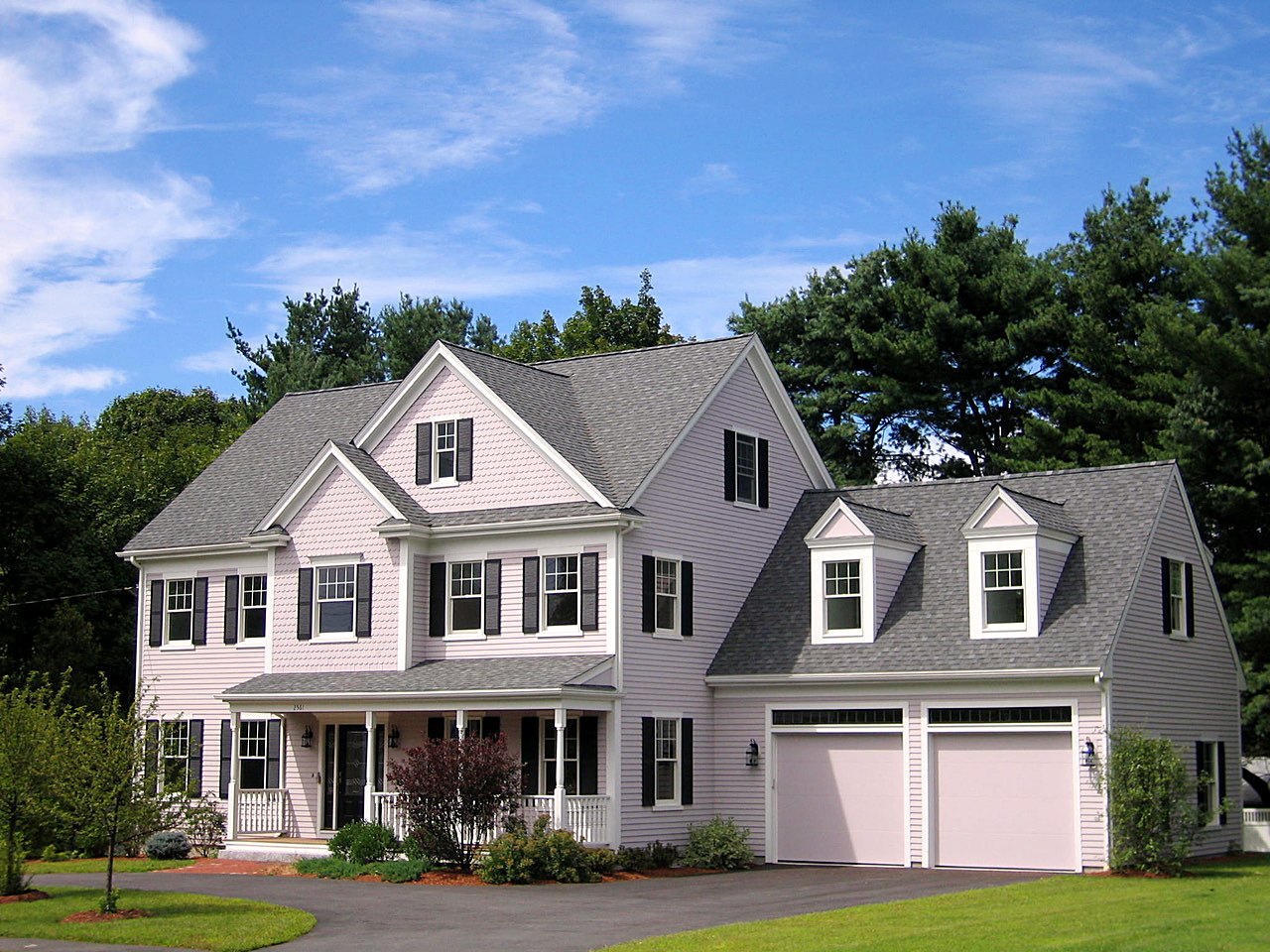 Colonial with shingled gables, black shutters, a covered porch and dormered two-car garage