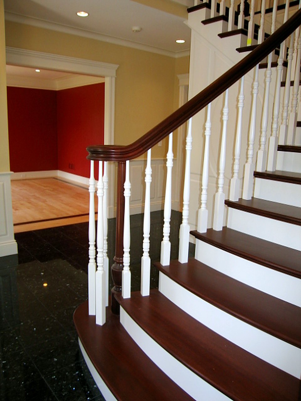 Curved foyer stair with turned balusters, a mahogany rail and treads over a granite floor