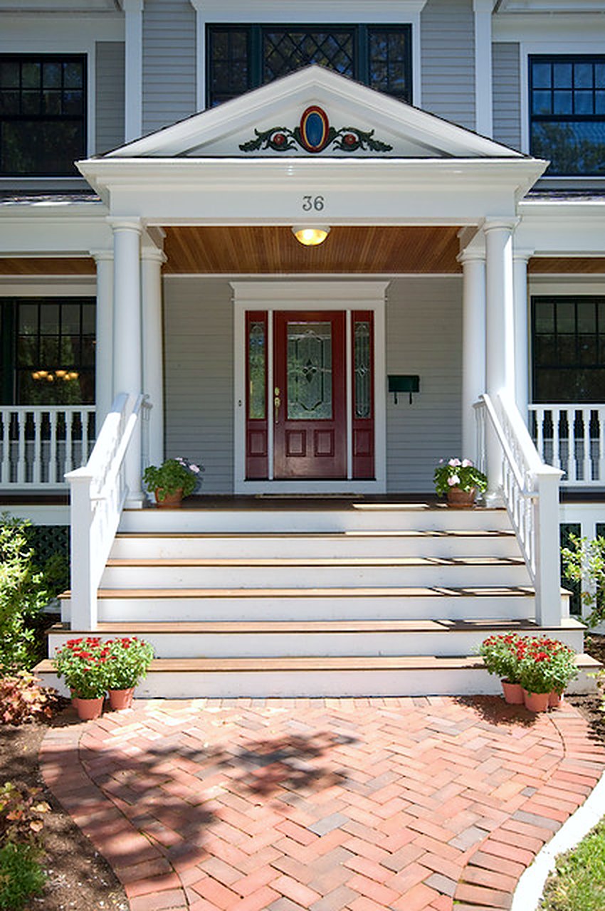 Front porch steps and pedimented entry with a red door and herringbone brick walk