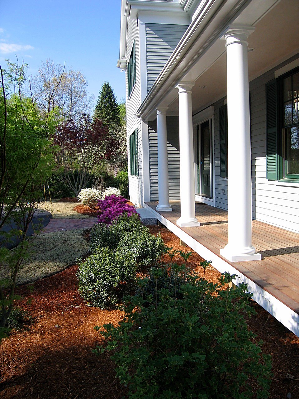 Front porch with Tuscan columns and mahogany decking beside new plantings