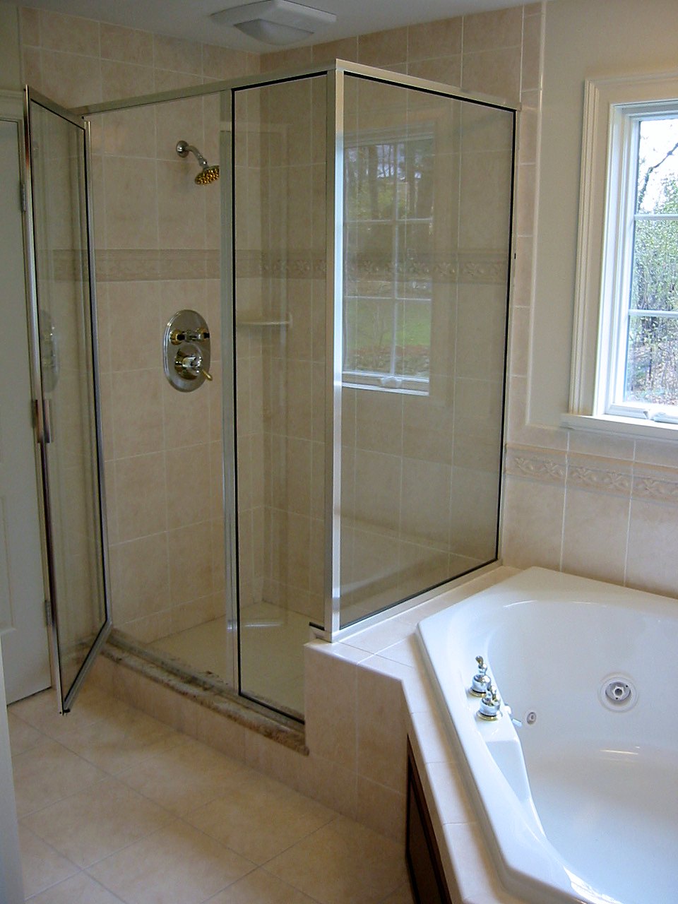 Glass shower enclosure beside a tiled corner whirlpool tub