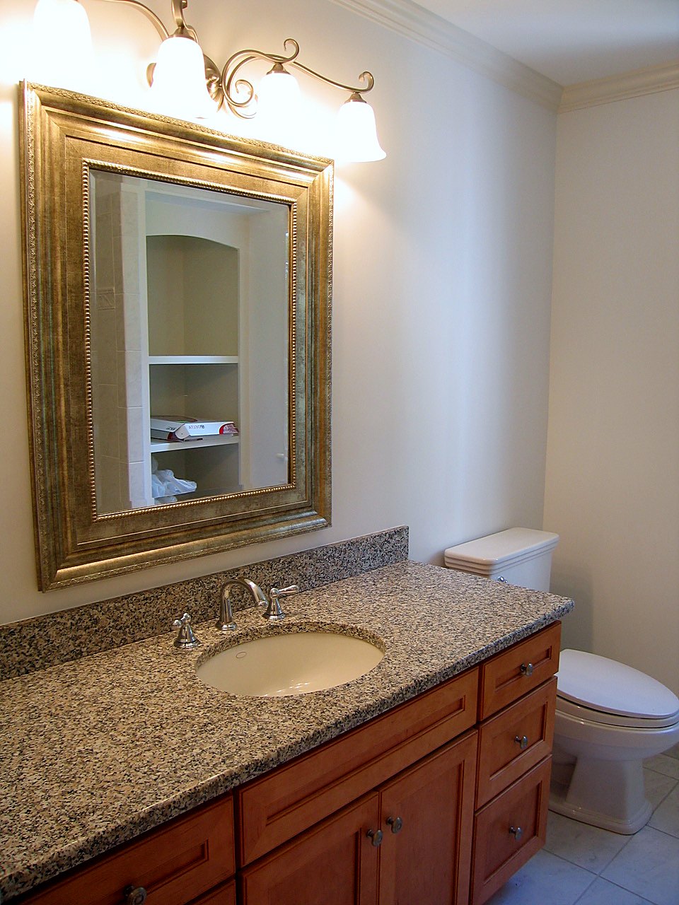 Maple vanity with a granite top under a gilt-framed mirror