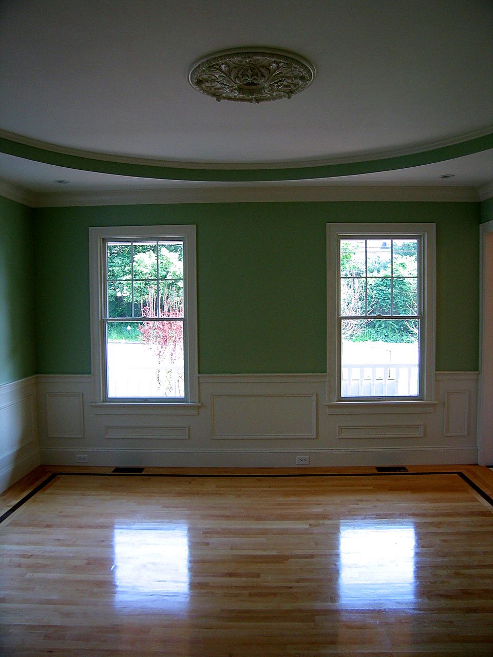 Oval-ceilinged room with a plaster medallion, paneled wainscot and a bordered maple floor