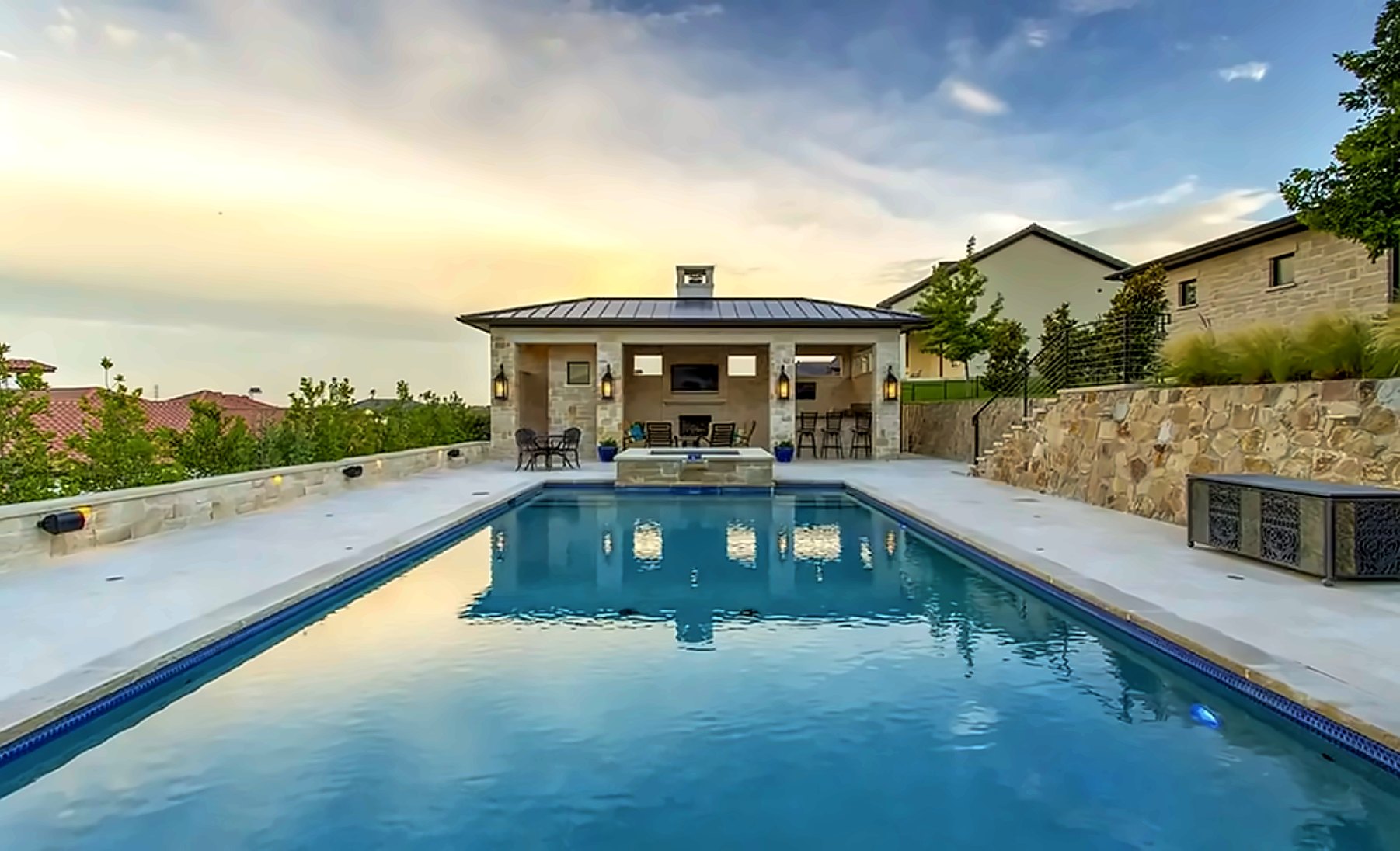 Pool and pavilion with an outdoor fireplace at sunset
