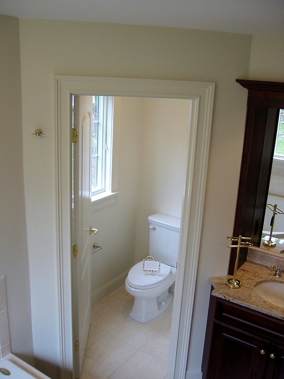 Private water closet seen through a cased doorway beside a cherry vanity