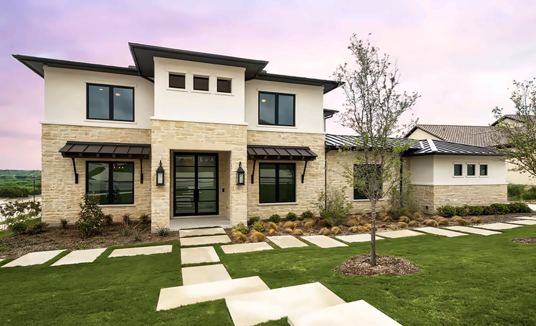 Stone and stucco contemporary home at dusk with a paver drive