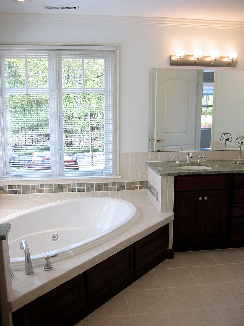 Tiled soaking tub with a slate accent band beside a cherry vanity