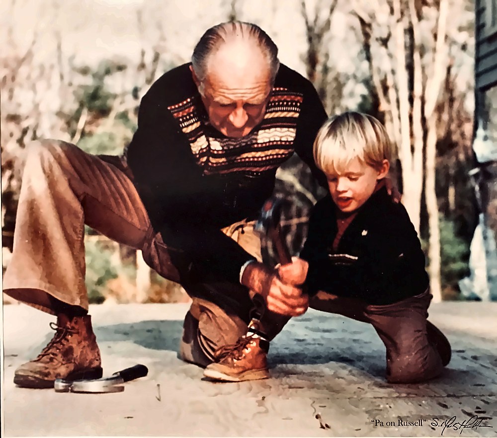 Vintage family photograph of a grandfather guiding a young boy as he swings a hammer on a wood porch