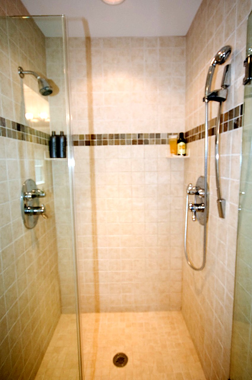 Walk-in tile shower with a mosaic accent band and hand shower